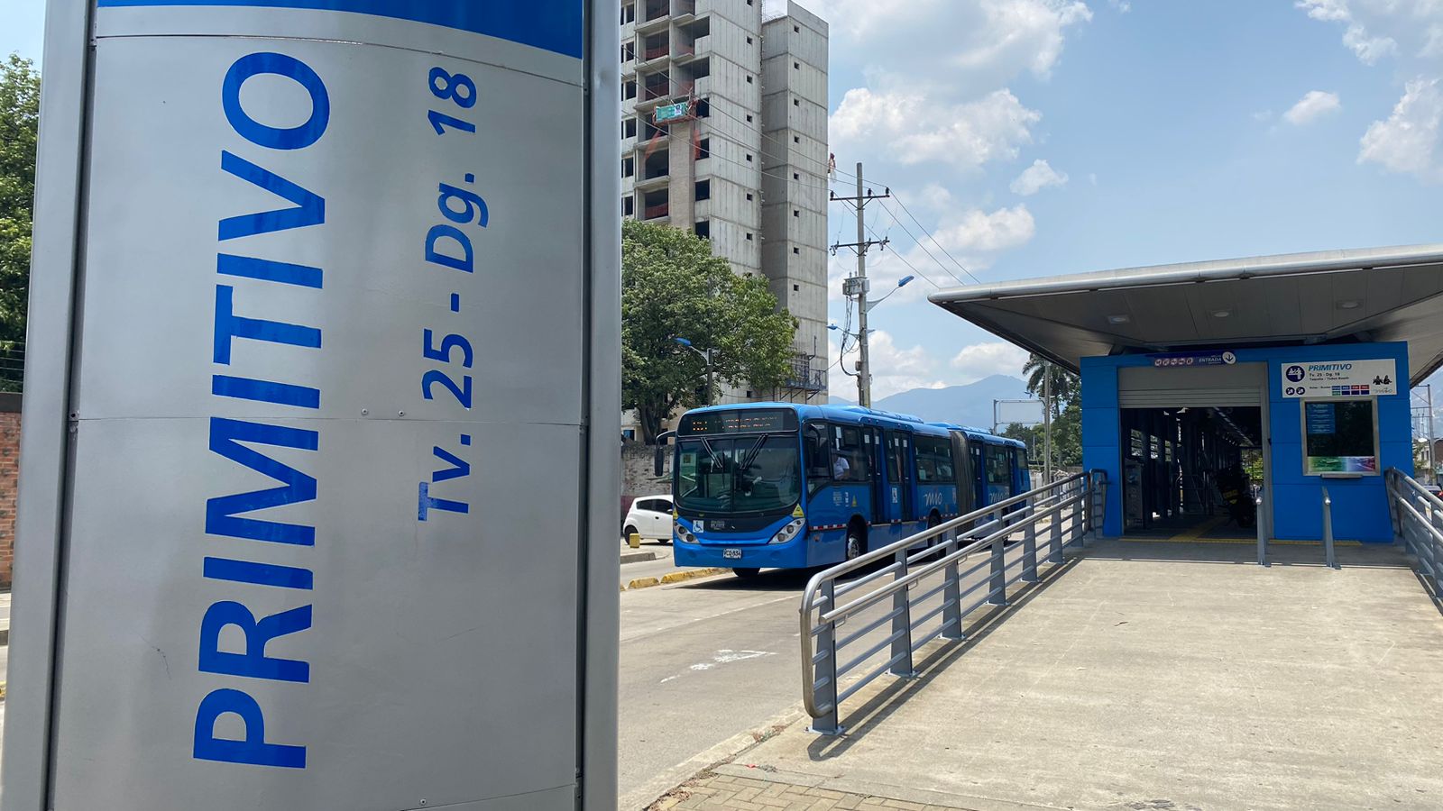 Foto donde se ve el mogador con el nombre de la estación Primitivo y la dirección. También sobre el carril del MIO un bus articulado y la entrada de la estación.