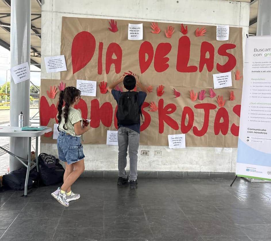 En este contexto se desarrolló la actividad “Mi mano dice NO”, en la cual una facilitadora invitó a los participantes a expresar, a través de un gesto simbólico, su rechazo al reclutamiento infantil. Para ello, se entregaron manos rojas elaboradas en cartulina que posteriormente fueron levantadas de manera colectiva mientras se compartía la frase: “Los niños no vamos a la guerra”.
